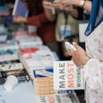 Livros expostos em uma feira literária, enquanto visitantes observam as publicações.