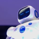 Robô humanoide moderno com rosto digital iluminado diante de uma tela tecnológica.