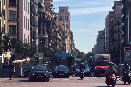 Rua movimentada de Barcelona com ônibus, carros e motos diante de edifícios urbanos.