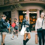 Pessoas de diferentes origens conversam e circulam em frente a um café em uma rua de Barcelona.