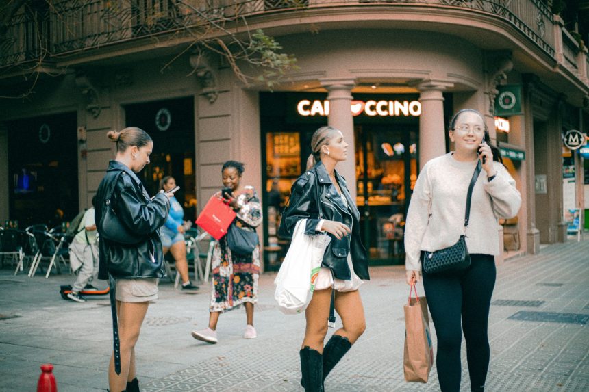 Pessoas de diferentes origens conversam e circulam em frente a um café em uma rua de Barcelona.