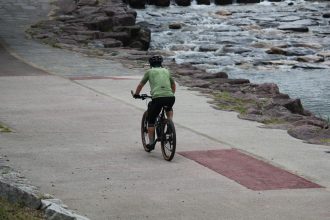 Ciclista percorre um caminho arborizado junto a um rio.