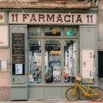 Fachada de uma farmácia tradicional em Barcelona, com letreiro clássico e bicicleta antiga na calçada.