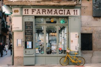 Fachada de uma farmácia tradicional em Barcelona, com letreiro clássico e bicicleta antiga na calçada.