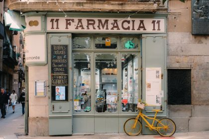 Fachada de uma farmácia tradicional em Barcelona, com letreiro clássico e bicicleta antiga na calçada.