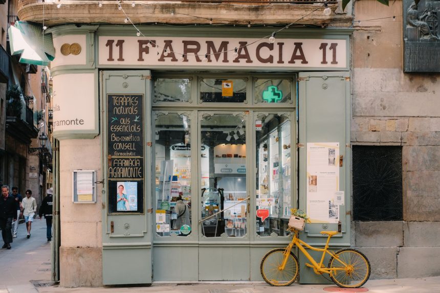 Fachada de uma farmácia tradicional em Barcelona, com letreiro clássico e bicicleta antiga na calçada.