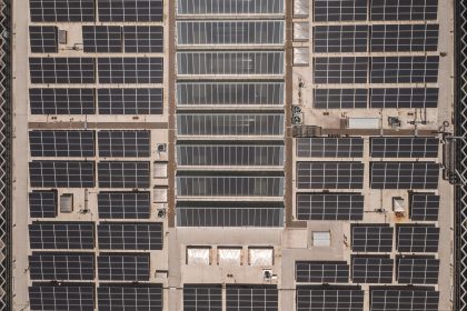 Vista aérea de uma ampla cobertura industrial coberta por fileiras de painéis solares.