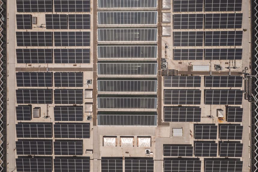 Vista aérea de uma ampla cobertura industrial coberta por fileiras de painéis solares.