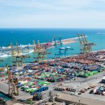 Vista aérea do Porto de Barcelona, com guindastes, contêineres e navios em uma área de operações portuárias.