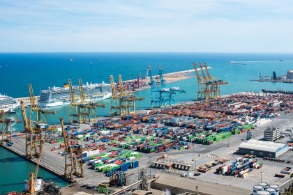Vista aérea do Porto de Barcelona, com guindastes, contêineres e navios em uma área de operações portuárias.