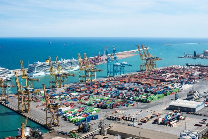 Vista aérea do Porto de Barcelona, com guindastes, contêineres e navios em uma área de operações portuárias.