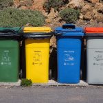Quatro contêineres para coleta seletiva de vidro, embalagens, papel e resíduos orgânicos em área externa