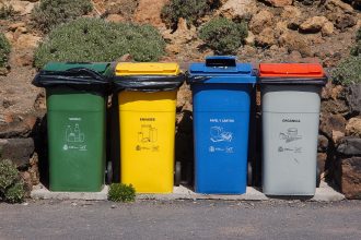 Quatro contêineres para coleta seletiva de vidro, embalagens, papel e resíduos orgânicos em área externa