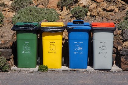 Quatro contêineres para coleta seletiva de vidro, embalagens, papel e resíduos orgânicos em área externa